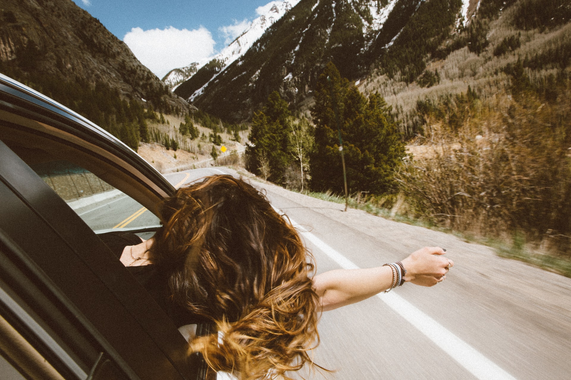 Girl sticking her head out the window on a road trip.