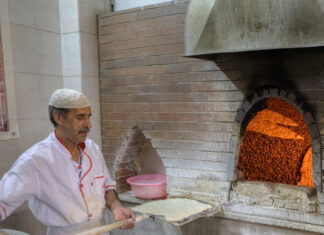 Baker with dough on a shovel stands near stone oven.